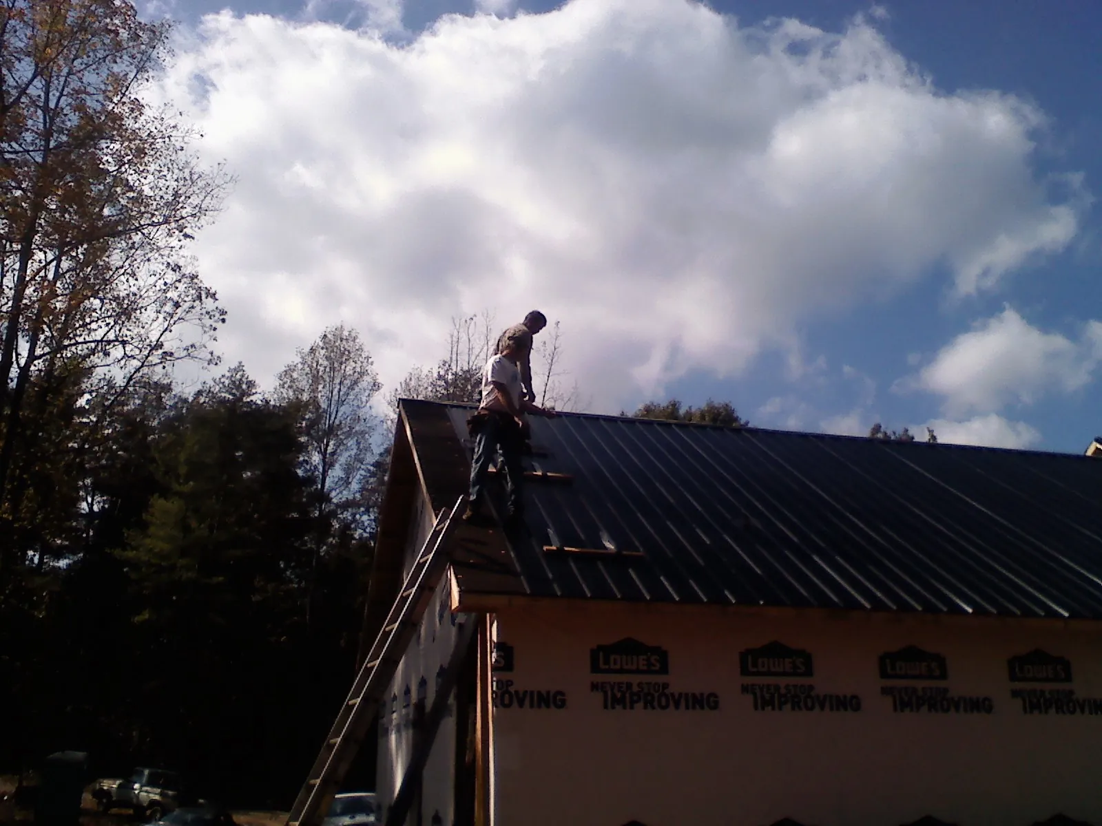 Roofer fastening dark metal panels high against a cloudy sky, from a Roof Inspection job in Troy